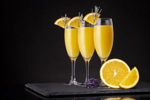 Mimosa cocktails in champagne glasses with orange juice and sparkling wine decorated with lavender leaves and orange slices. Focus on the right glass