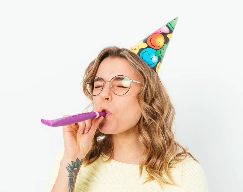 a young woman with a party hat blowing a noisemaker